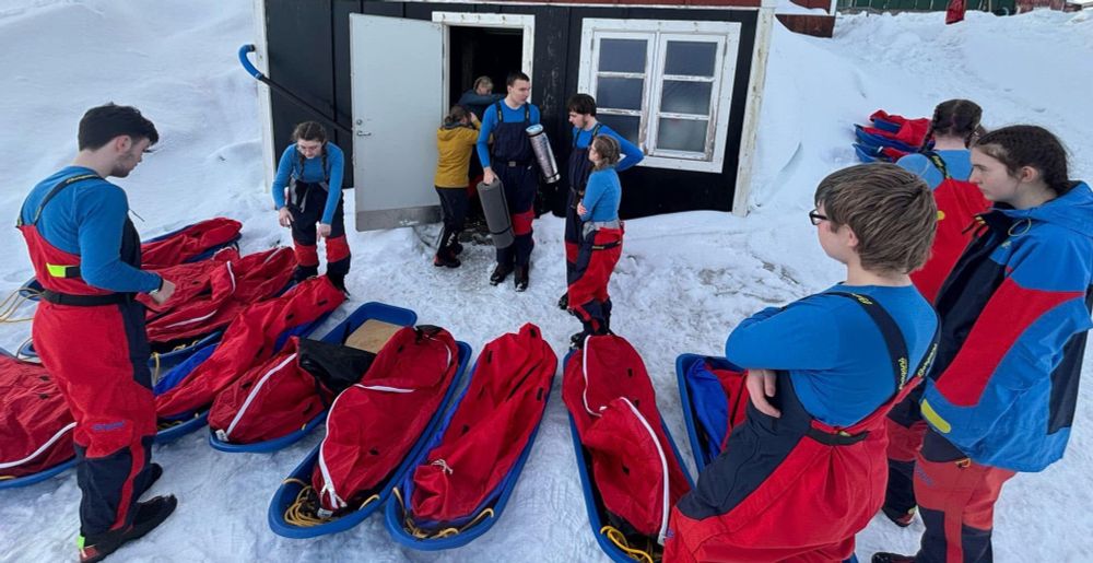 9 pupils take out sledges from a store house surrounded by snow. 