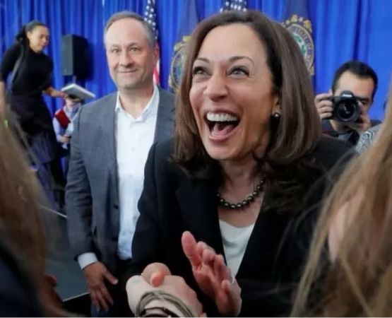 Kamala Harris, smiling broadly as she grasps someone's hand. Doug Emhoff is in the background, looking just a little goofy.