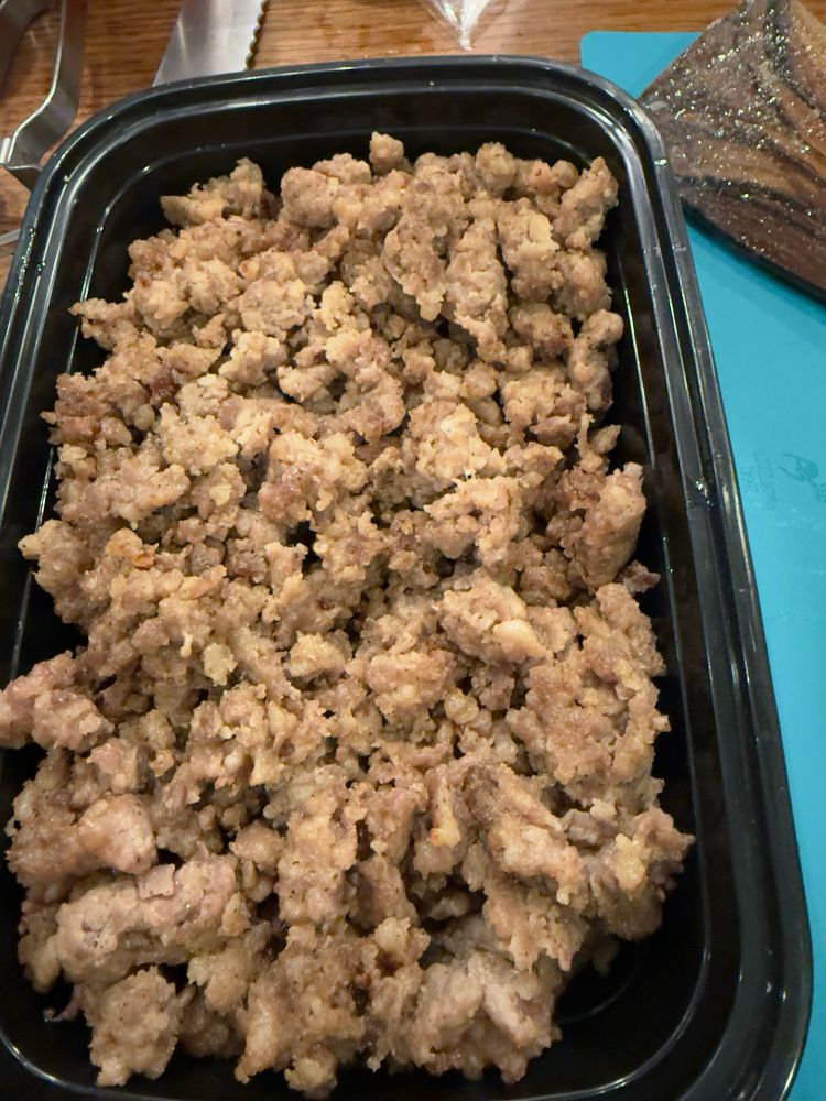 A black, rectangular container filled with crumbled cooked sausage. 