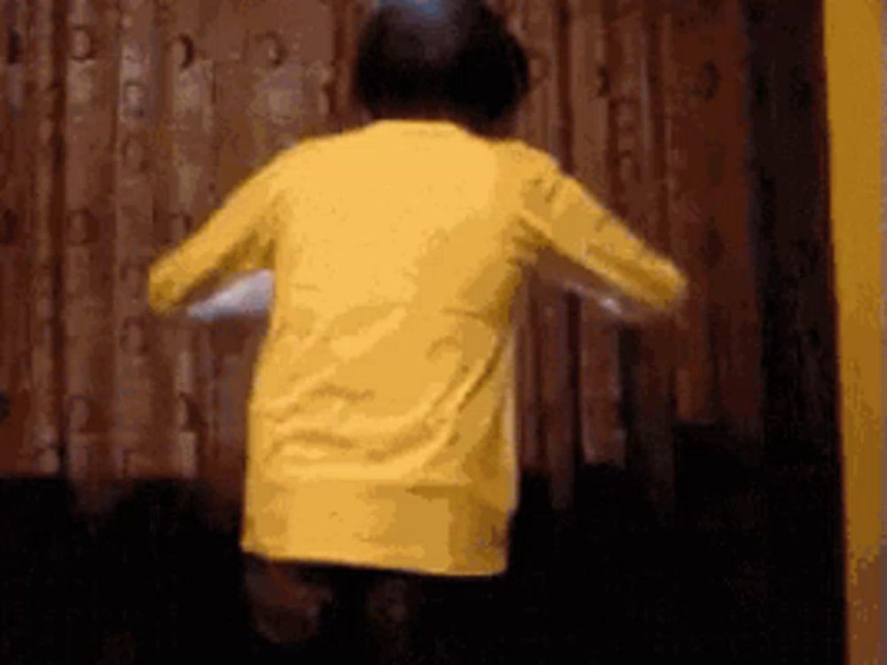 a boy in a yellow shirt is dancing in front of a wooden wall .