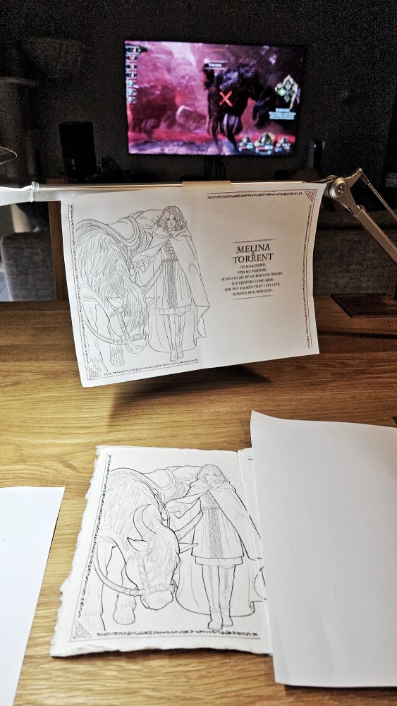 A photo of a dining table with a work in progress drawing over it and a reference drawing hanging from the lamp. The TV is in the background displaying Expedition 33 videogame.