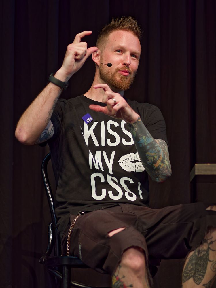 A photo of Adam sitting, talking, and gesticulating, showing something with his fingers.