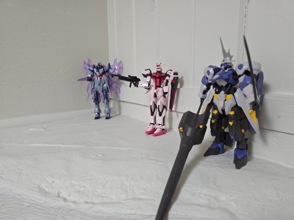 Three gundam mechs on a white pillar with a white background