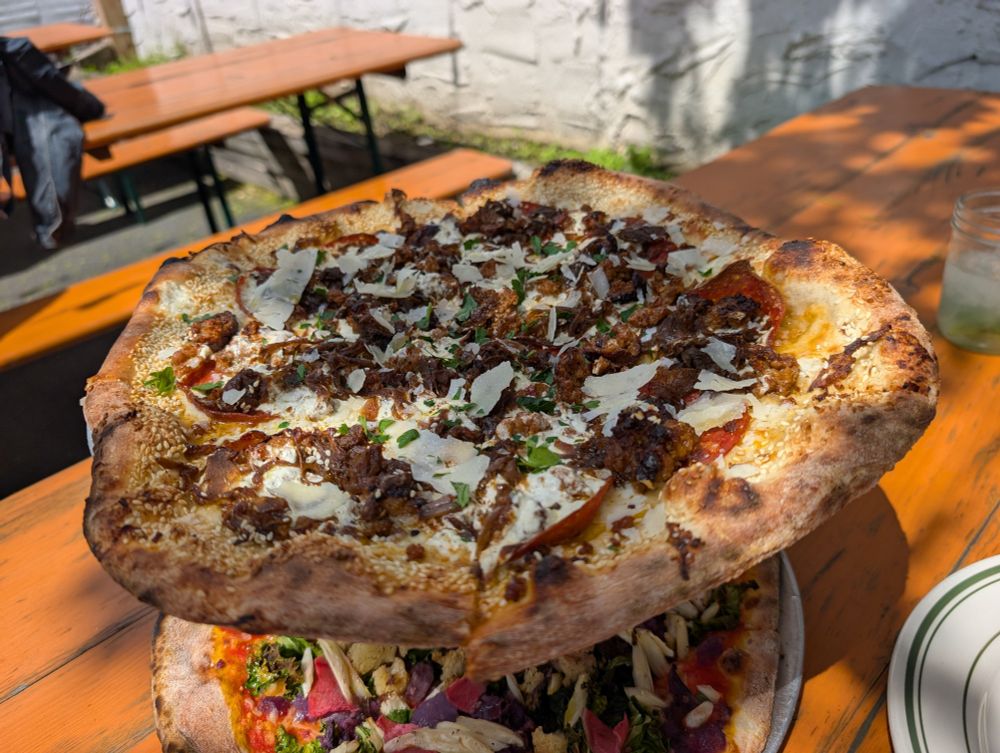 White pizza with pepperoni and sausage sitting on a little pizza shelf thingy with a veggie pie beneath it 