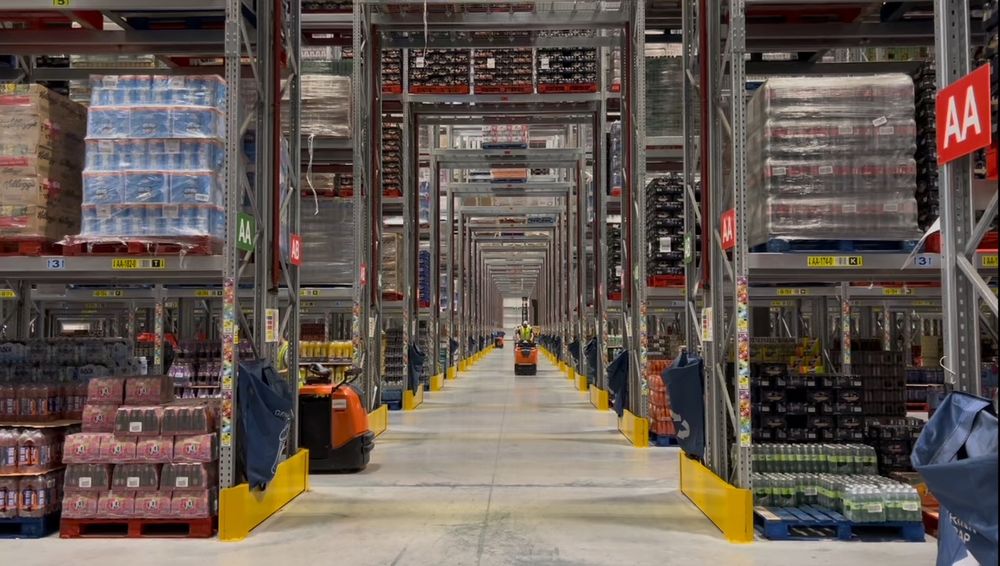 A forklift truck in the distance between giant shelves at the Iceland depot