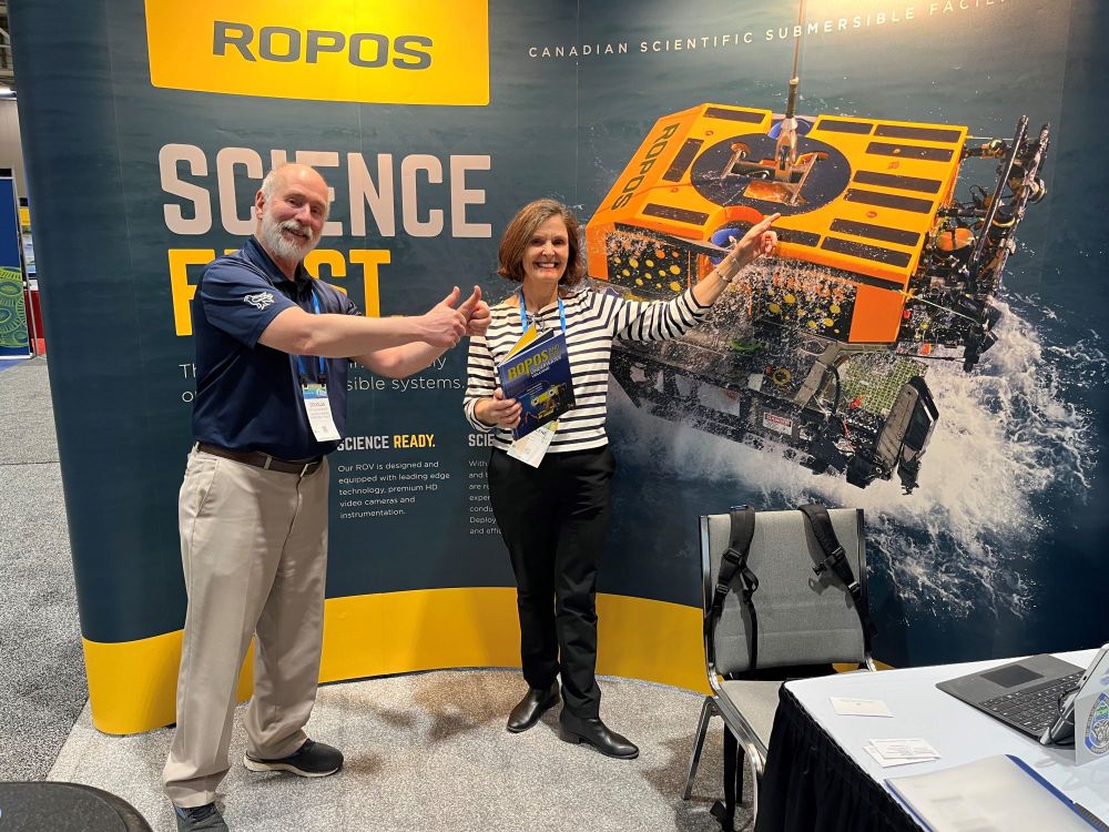 Doug Bancroft and a conference attendee posing happily in front of the CSSF ROPOS booth, pointing at the photo of ROPOS and giving a double thumbs up.