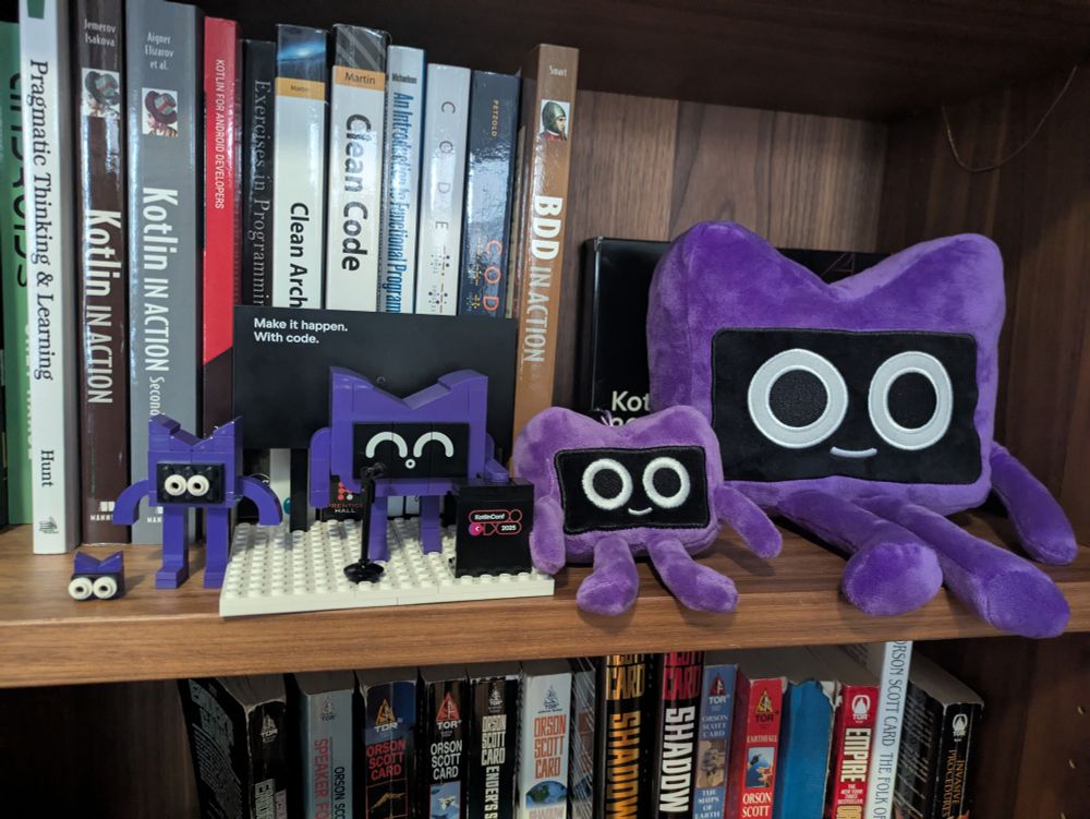 Multiple Kodees on a bookshelf, including two different sizes of plush and three different Lego versions.