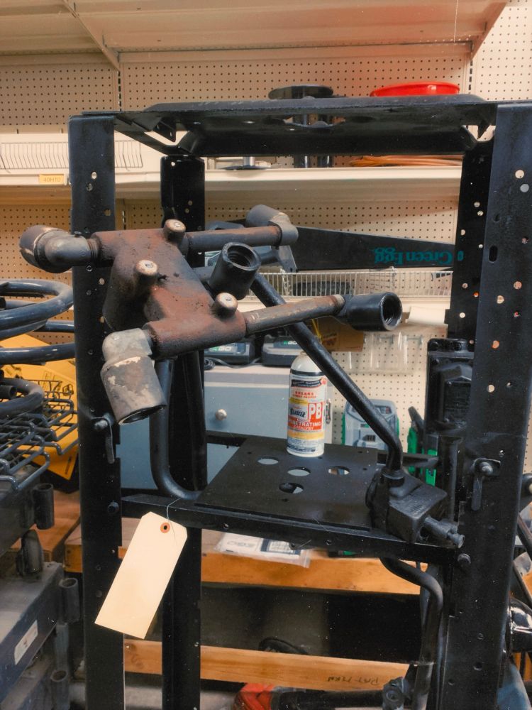 I black metal framework that’s nearly 6 feet tall with a vintage plumbing pipe style system run through it that ends in light sockets. Somewhat rusty and definitely old, I’m told it’s part of a vintage advertising display. A bottle of penetrating oil sits on the shelf inside it, around it is a workshop