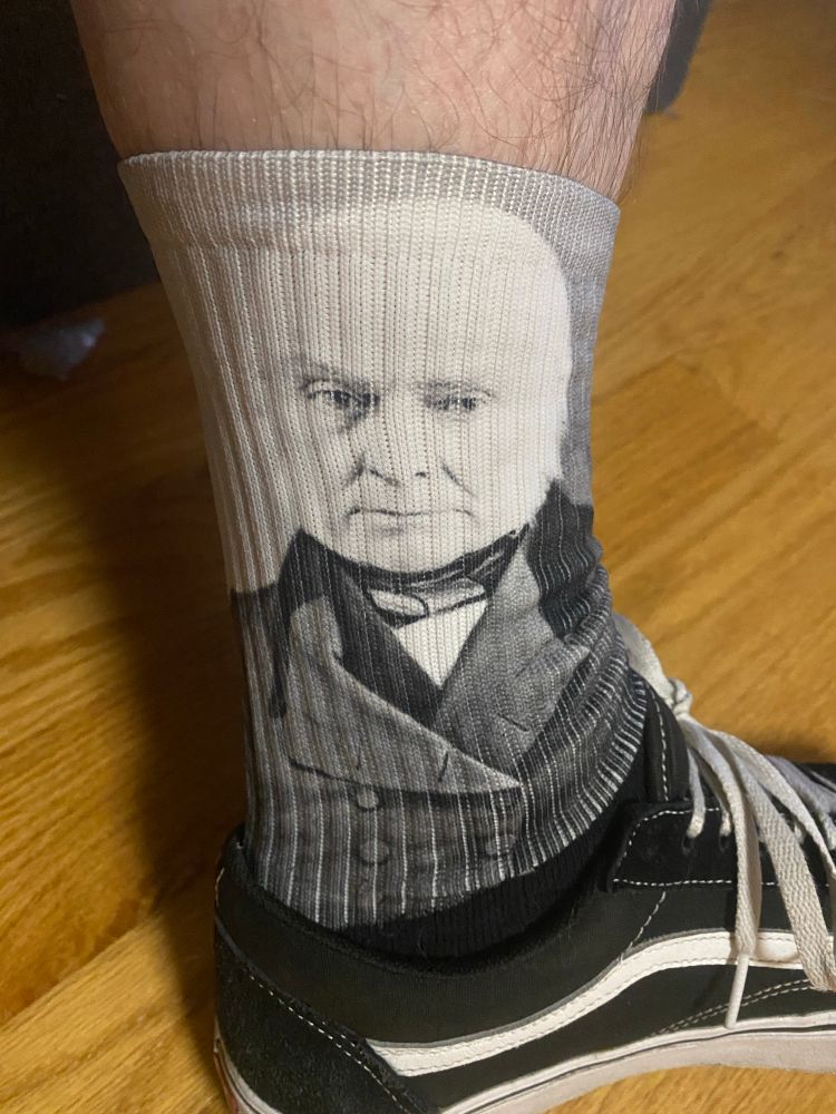 A picture of my leg with my socks pulled all the way up. The face of John Quincy Adams is shown on the socks.