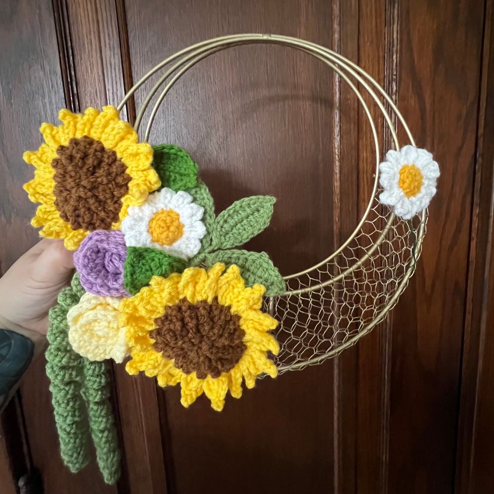 Gold crescent basket with crocheted sunflowers, daisies, & two roses placed on the left. Unfinished work. 
