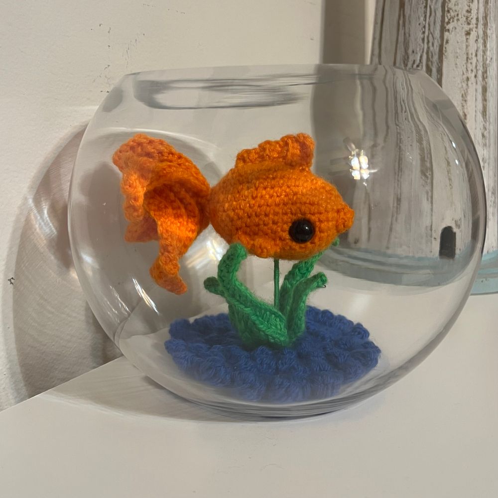 Crocheted goldfish in a glass fishbowl.