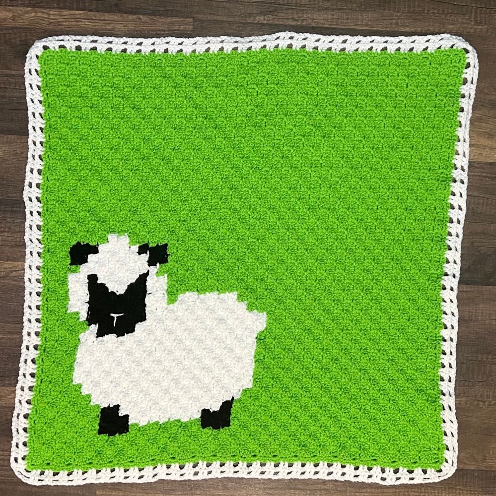 Crocheted baby blanket in green with a sheep in the lower left hand corner. 
