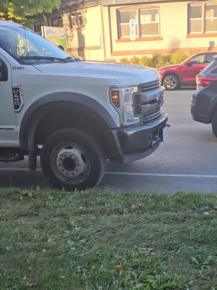 White Ford F450 pickup truck stopped in a bike lane next to a grass boulevard.