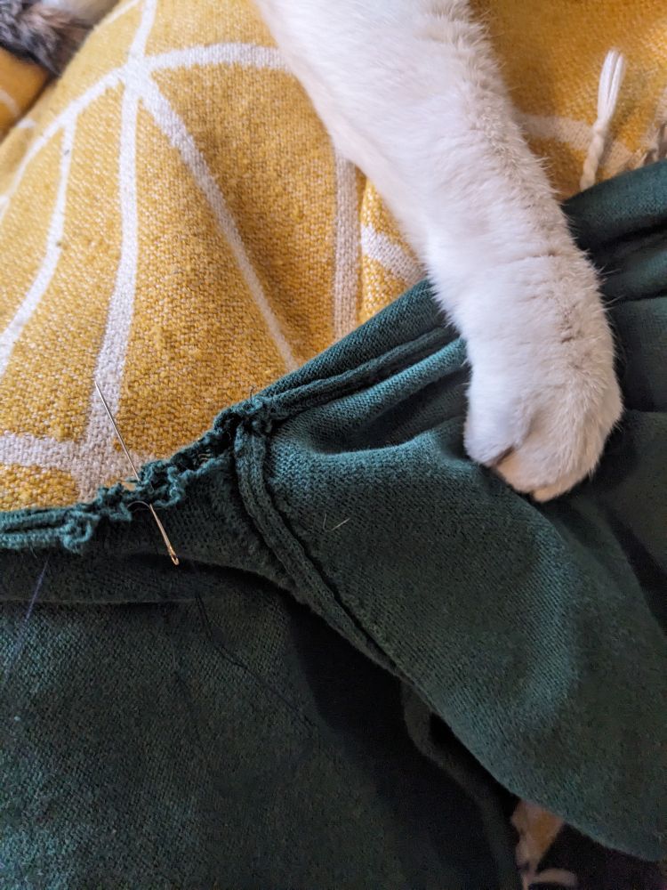 A green jumper being sewn with a cats' paw resting on the arm