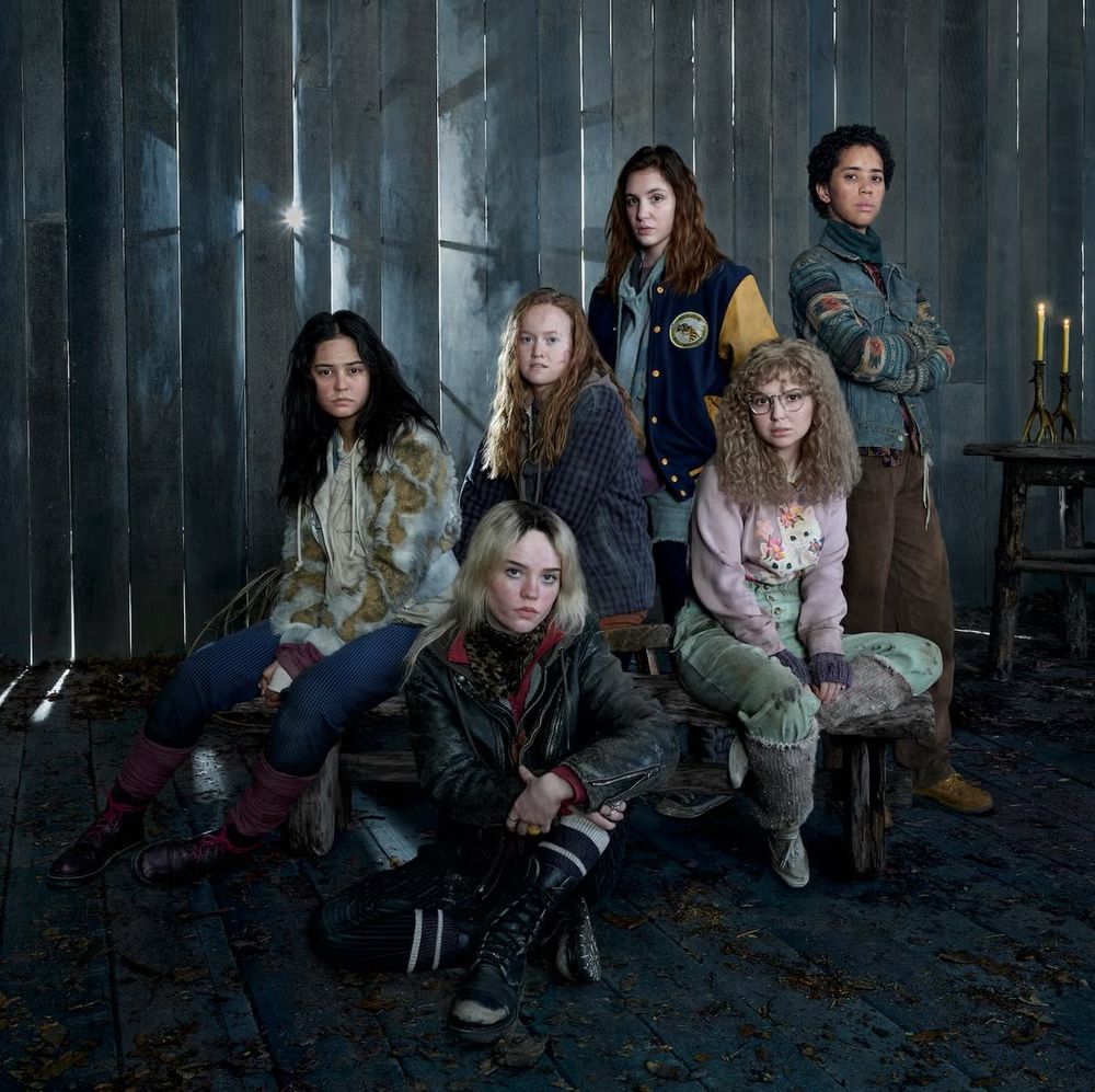 Six women pose for a promotional shot in front of a dark forest. 
