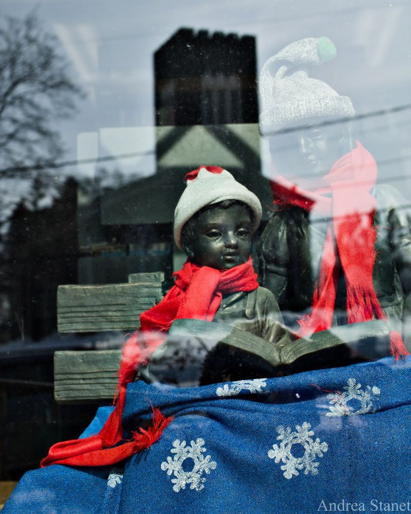 Image of statue of little boy in a scarf with a building reflected in glass behind him