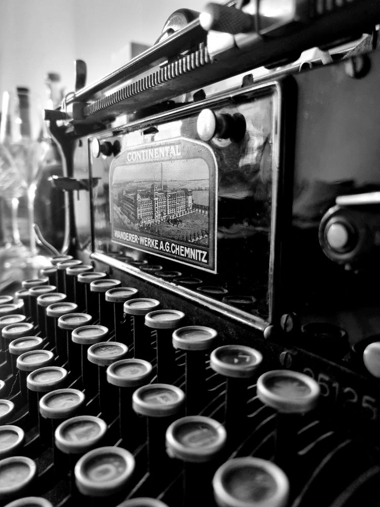 Nahaufnahme von der Seite einer alten Schreibmaschine aus schwarz lackiertem Metall, man sieht die runden Tasten und das Typenschild mit der Aufschrift: Continental Wanderer-Werke A. G. Chemnitz