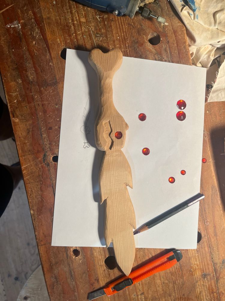 Wood carved into a sword similar to what the previous drawing instructed, surrounded by red plastic gemstones 