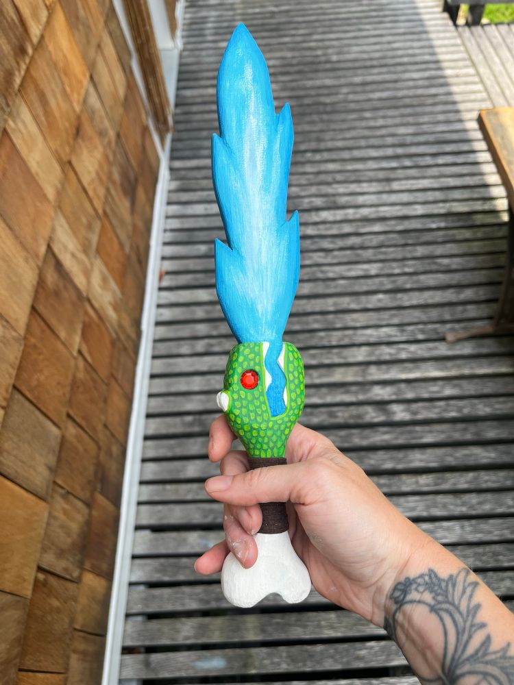 The finished sword, painted blue and green and white, with a cord wrapped handle and a red gemstone eye