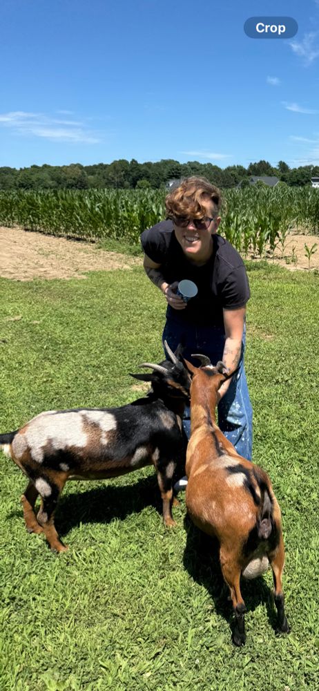 Lucy grinning while feeding two goats