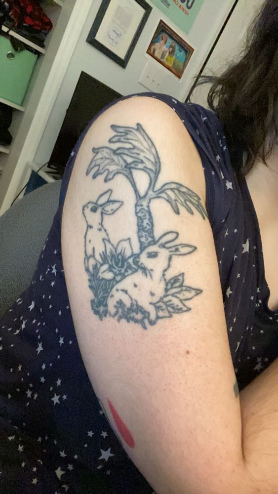 An upper arm/shoulder tattoo of two rabbits, a palm tree, and foliage from the inside cover of Authority by Jeff Vandermeer