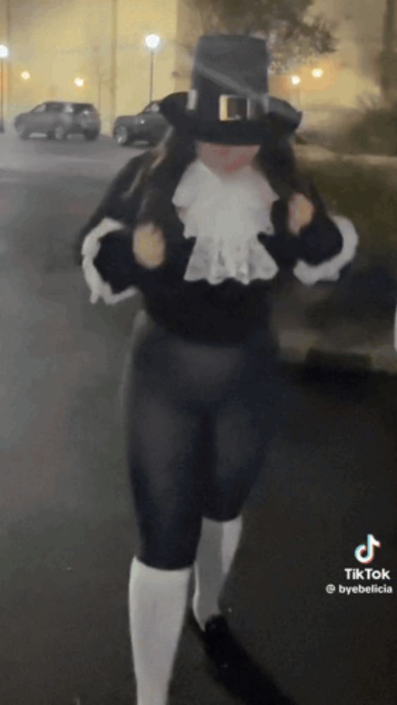 a woman in a pilgrim costume is walking down a street at night