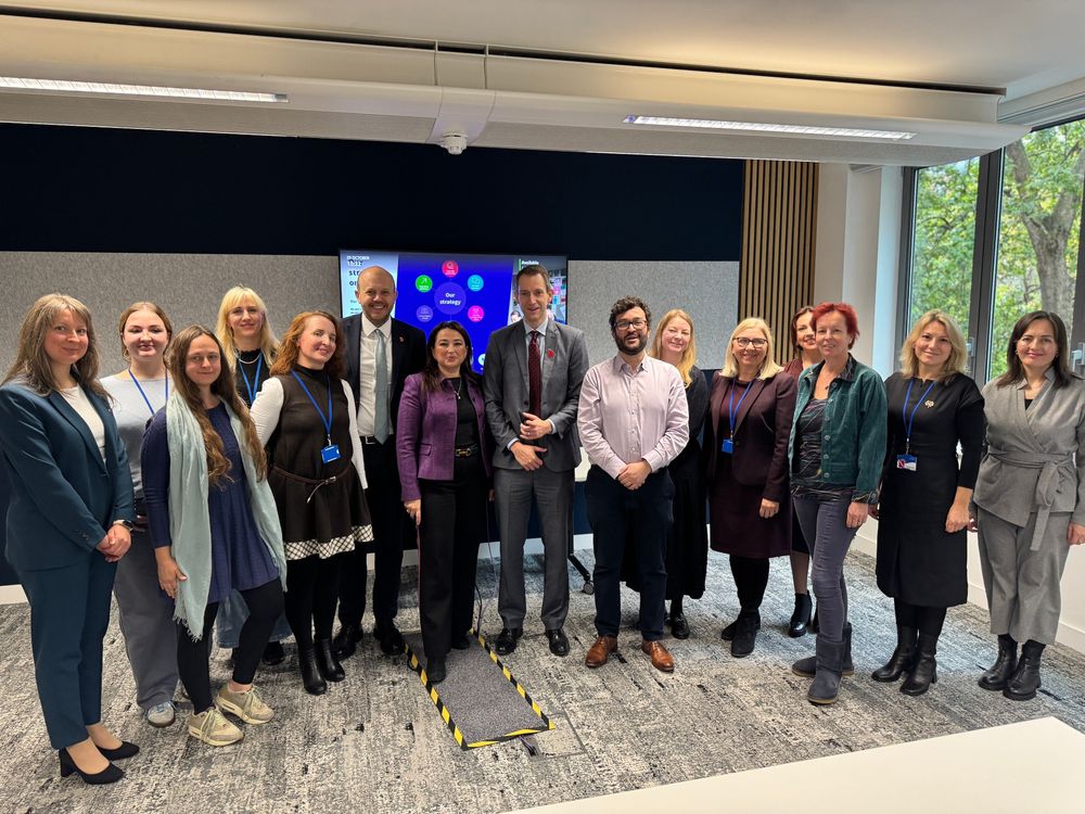 Fifteen people lined up facing the camera in a room. 