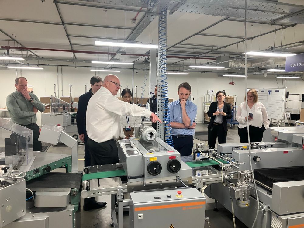 A man in a white shirt pointing at a machine with several other people present.