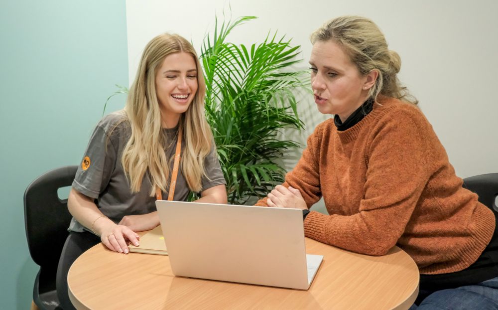 Two women at a desk looking at a laptop. 