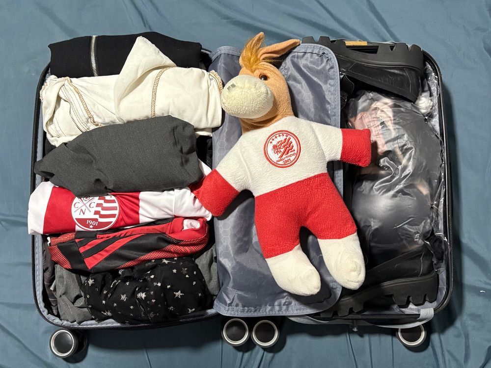 mala aberta com diversas roupas guardadas, dentro dela também está uma pelúcia de cavalinho usando o escudo do náutico. 