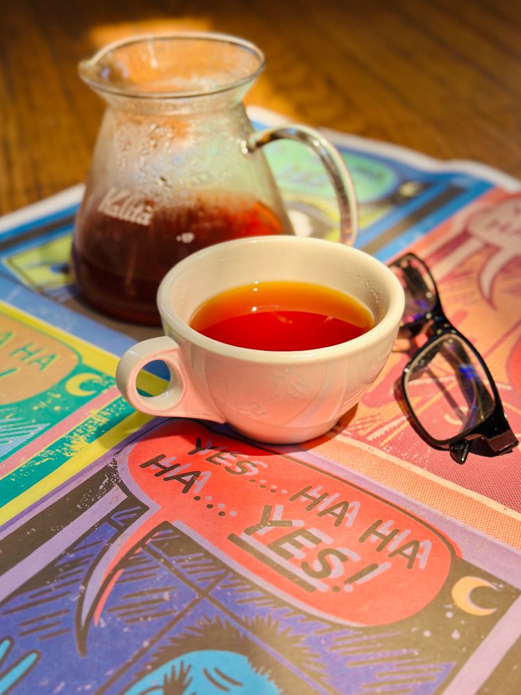 a sunlit cup of coffee and reading glasses atop a page from The Onion newspaper reading "YES... HA HA HA... YES!"