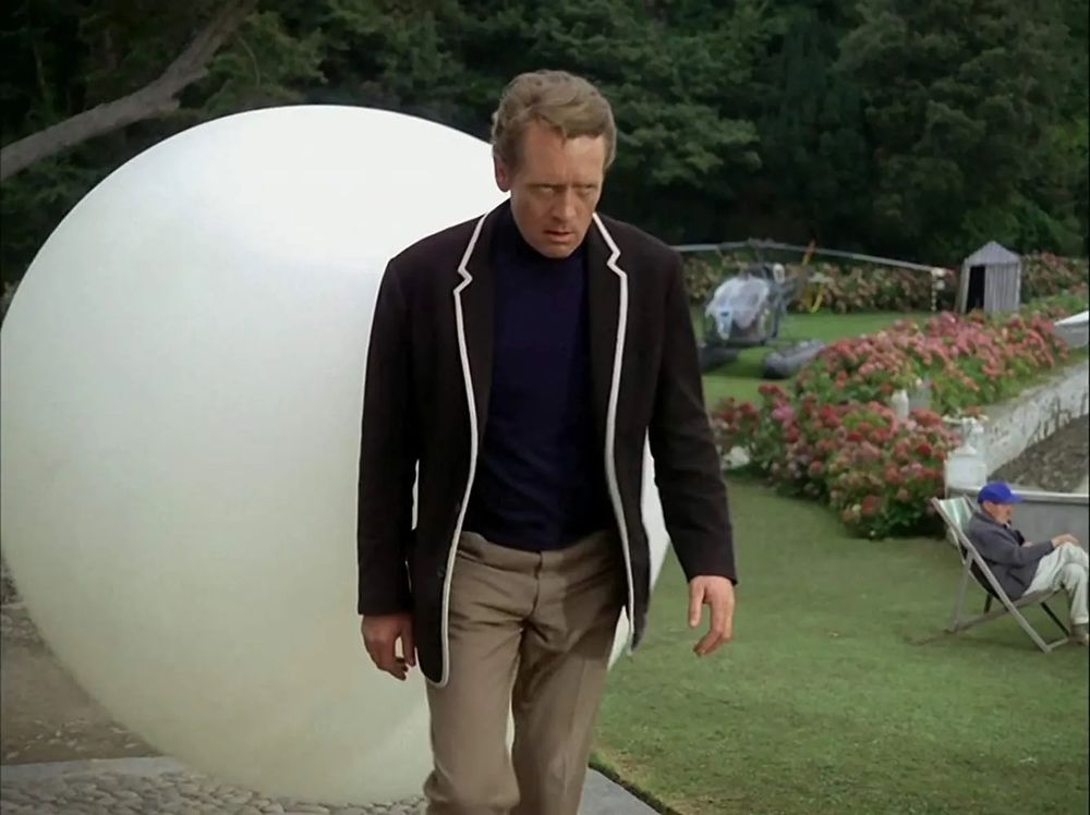 A seething number 6 gets escorted back to the village by a giant white ball