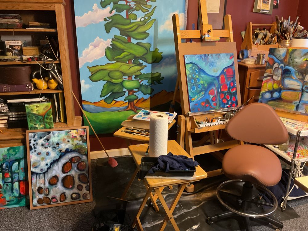 Art studio space with easel and several paintings at different stages. 