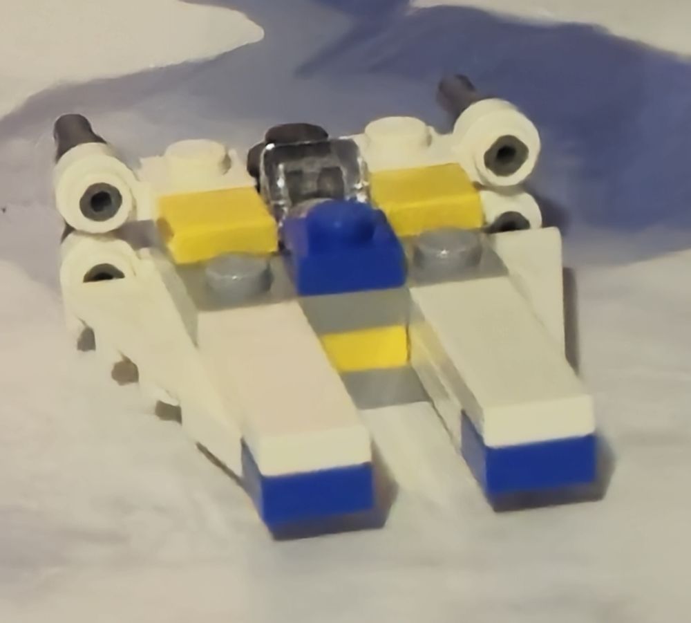 Miniature Lego Space Ship. It is white, with yellow and blue highlights. It is shaped like a 2 pronged fork.