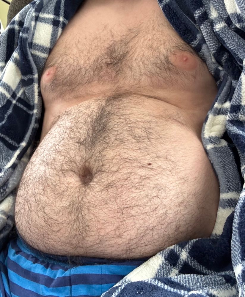 Hairy man sitting in a recliner wearing a blue robe and boxers, his robe fully open to show his belly and chest