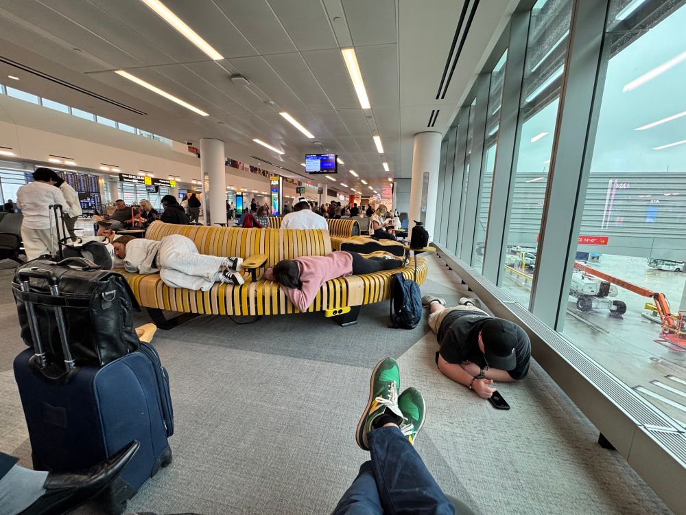 Two people lay down asleep on uncomfortable wooden benches, taking up six seats, while another United flyer lays belly down on the floor on his phone. Weird