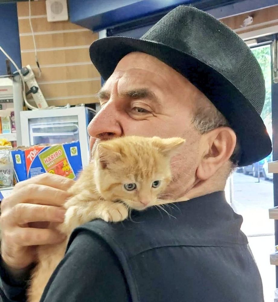 Ginger kitten on the shoulder of a man with black hat 