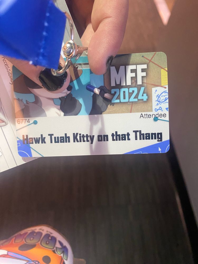 Con badge saying “hawk tuah kitty on that thing”
