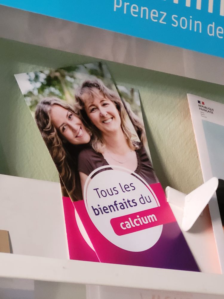 photo ultra zoomée d'une brochure chez mon médecin
sur la partie supérieure on voit 2 femmes blanches, cheveux longs blonds, l'une devant l'autre. La femme de derrière a sa tête posée sur l'épaule de celle de devant, on dirait qu'elles s'enlacent. Elles sourient.
Sur la moitié inférieure dégradé de couleur de haut en bas rose puis biolet foncé avec par dessus un cercle blanc sur lequel est marqué "Tous les bienfaits du calcium"