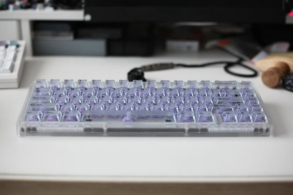teclado mecânico sobre uma mesa, corpo e teclas transparentes, mostram switches roxos dentro dele