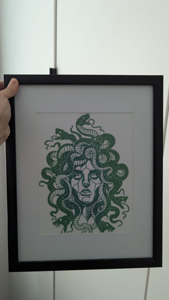 A green linocut of Medusa. Her snakes coil, open-mouthed, in every direction.