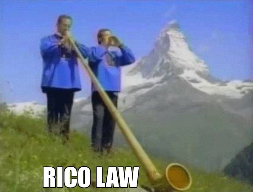Picture of two men on a hill in the Swiss Alps, one playing an alphorn, as seen in a Ricola cough drops commercial with the caption "RICO LAW"