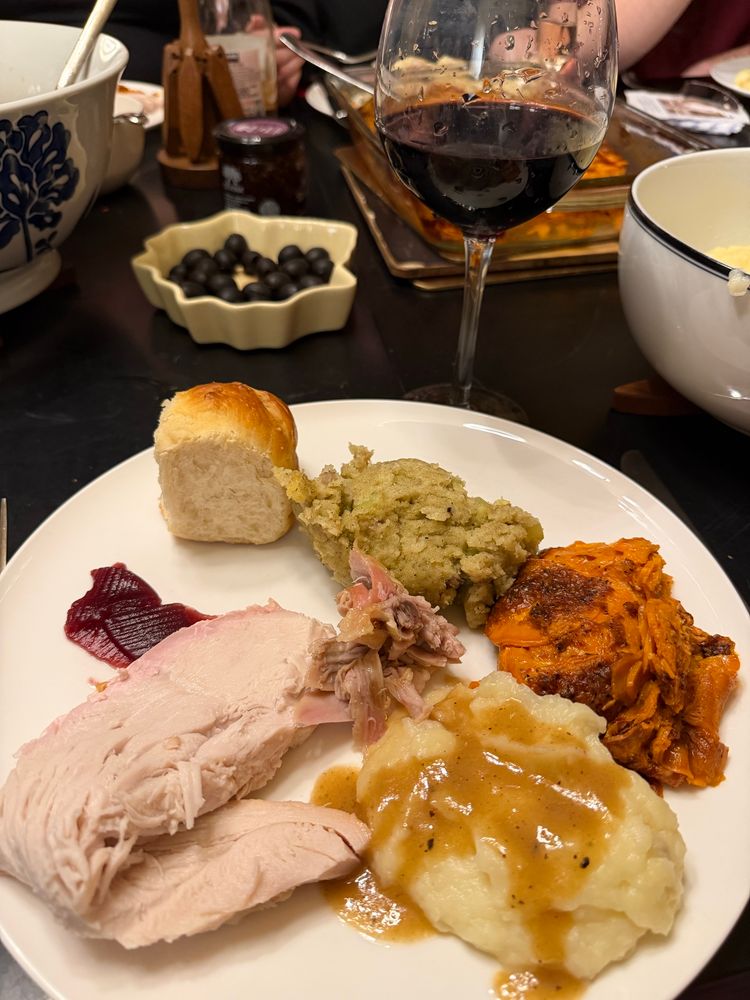 A picture of a dinner plate with turkey, mashed potatoes with gravy, sweet potato casserole, stuffing, a roll, and some cranberry sauce 