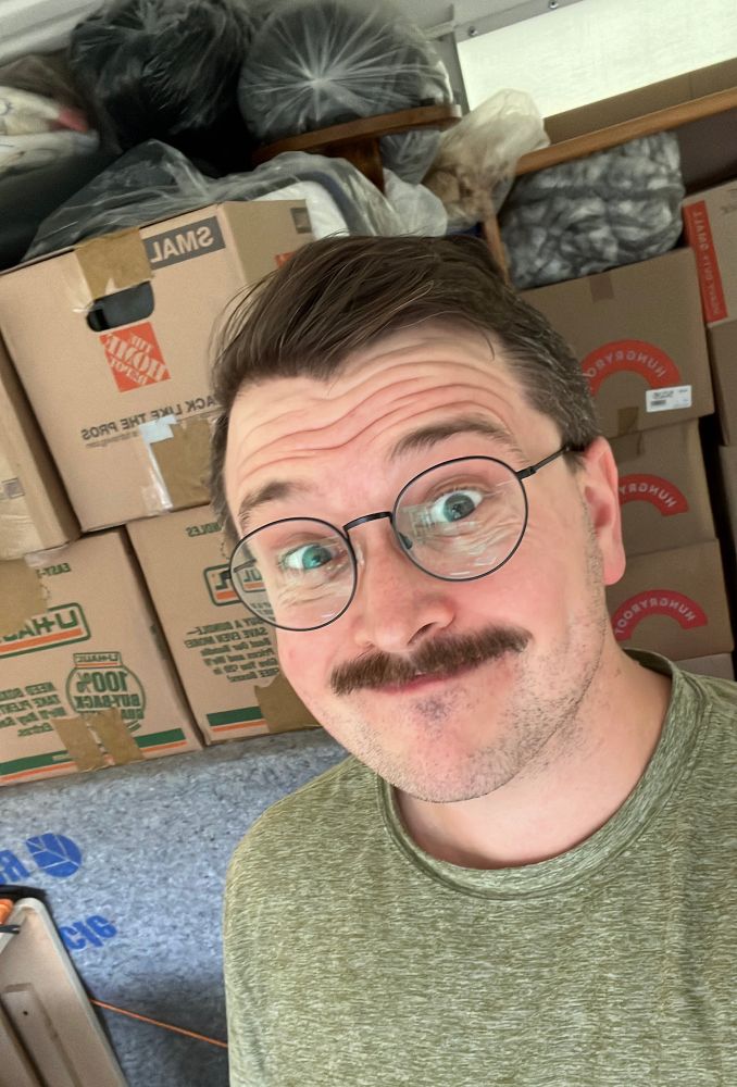 Me smirking as I stand in front of a wall of boxes 