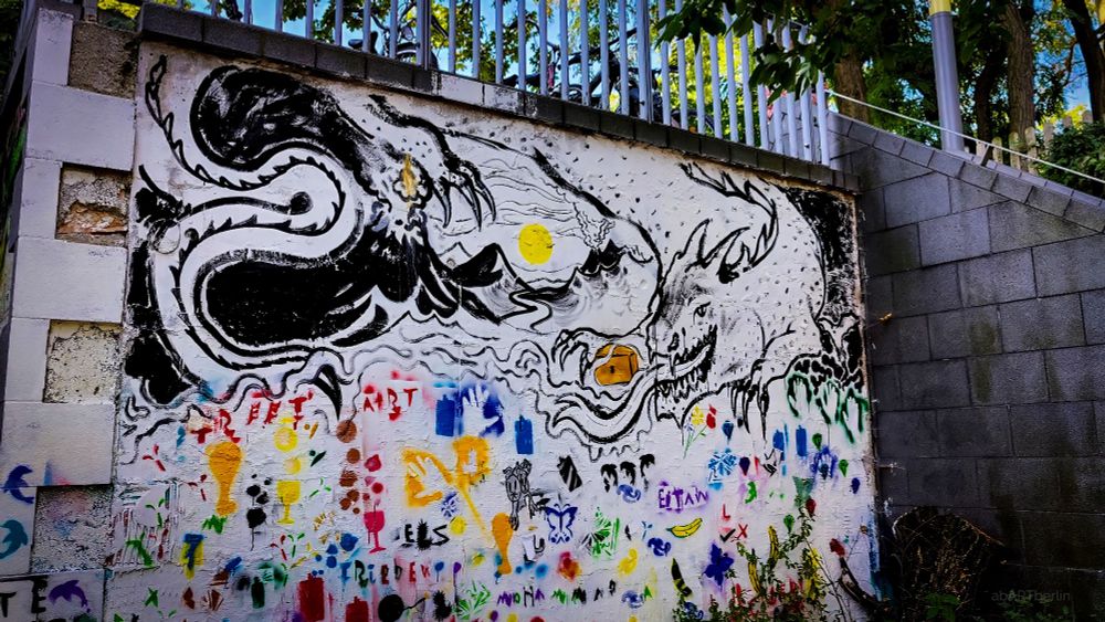 Foto von einer Mauer. Zu sehen sind darauf viele einzelne, kleine Grafftis, chaotisch und bunt.