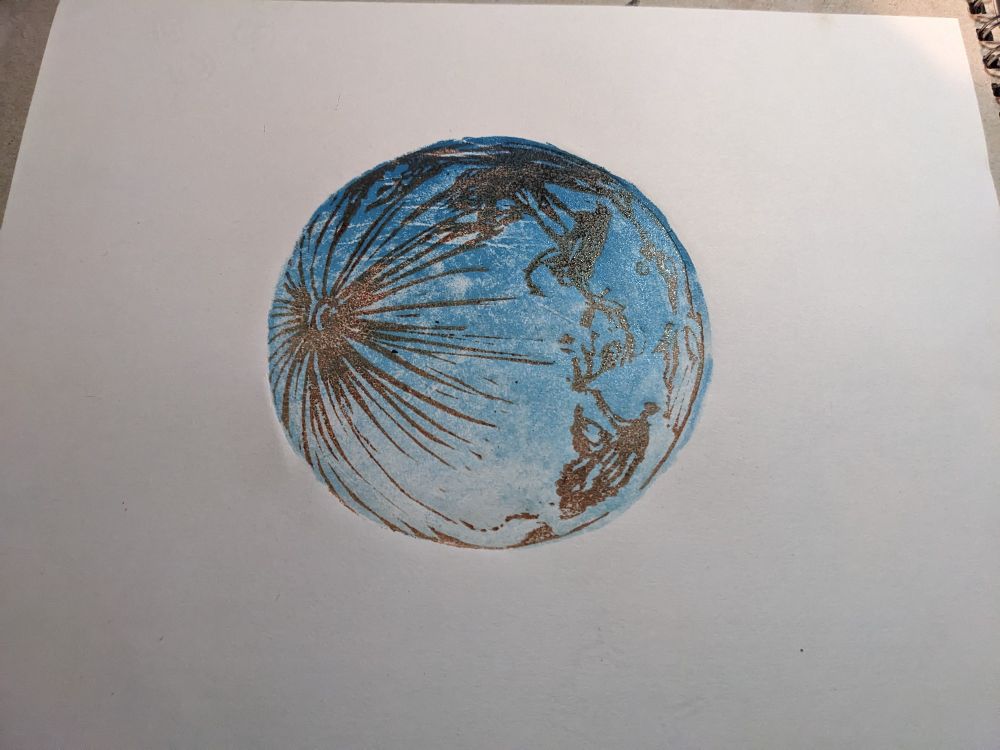 A blue and brown print of a planet. Brown lines radiate from an impact site on one side, the base colour of the planet is light blue.