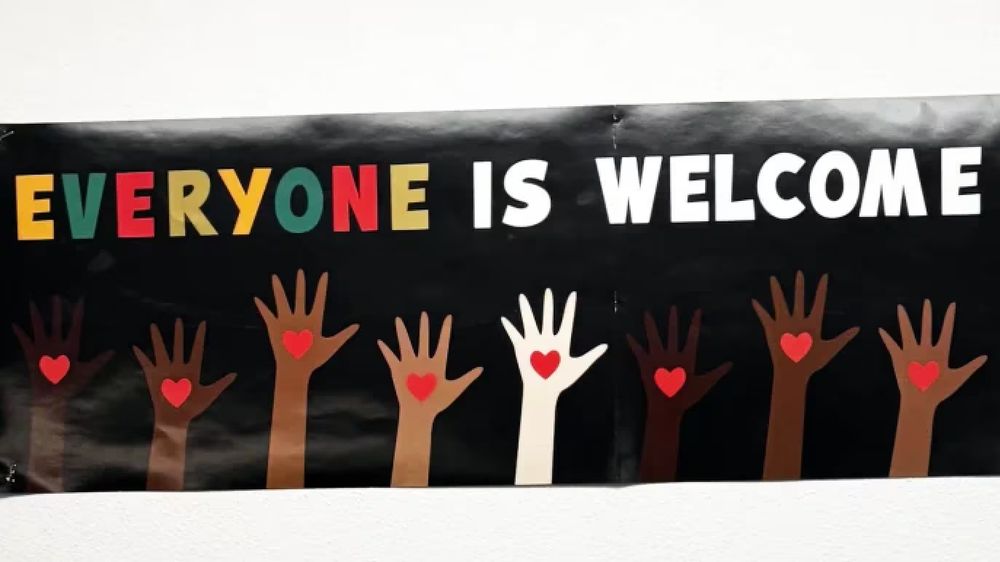 A poster that says "everyone is welcome here" with hands help up, drawn in several different skin tones. A teacher was ordered to take it down from her classroom because the sentiment was "her opinion" and not endorsed by her school.