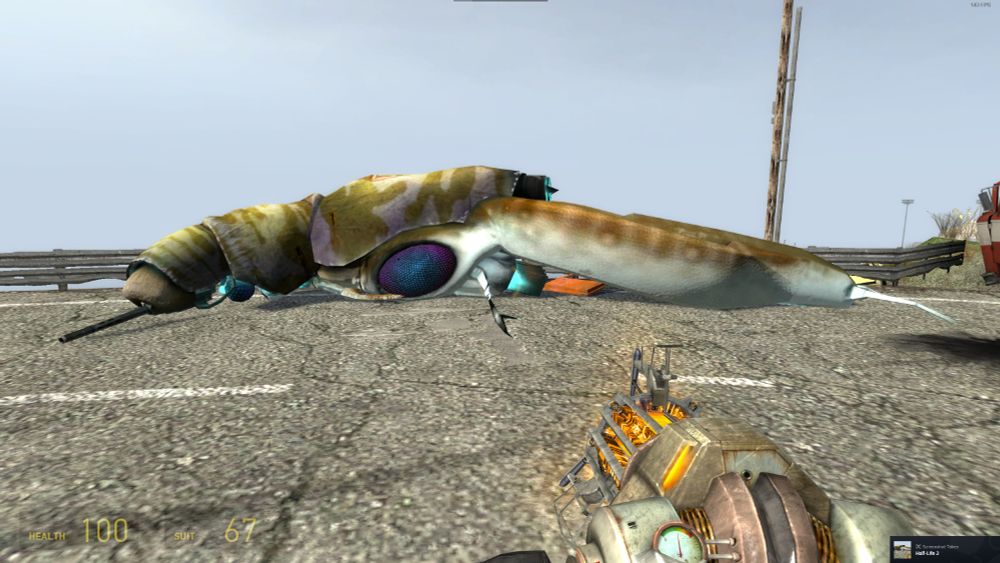screenshot of the video game Half Life 2. A massive, insectoid, organic helicopter creature lies dead and stretched out across a length of highway with a beach in the background. Massive blue scintillating eyes dot its piebald, shelled carapace. It has a gun fitted into its head, a huge organic rotor of dragonfly wings in the rear, blue-hot jet engines on the underside, and is decked with finlike winglets along its sides. There's a small, exposed brainstem with two large compound eyes near the front, behind the gun. 