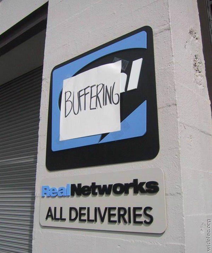 Outdoor sign reading "RealNetworks - All Deliveries" covered by a handwritten sign that says "BUFFERING"