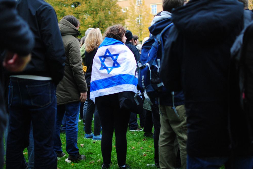 Ein Mensch gehüllt in eine Israelfahne inmitten von anderen Menschen.